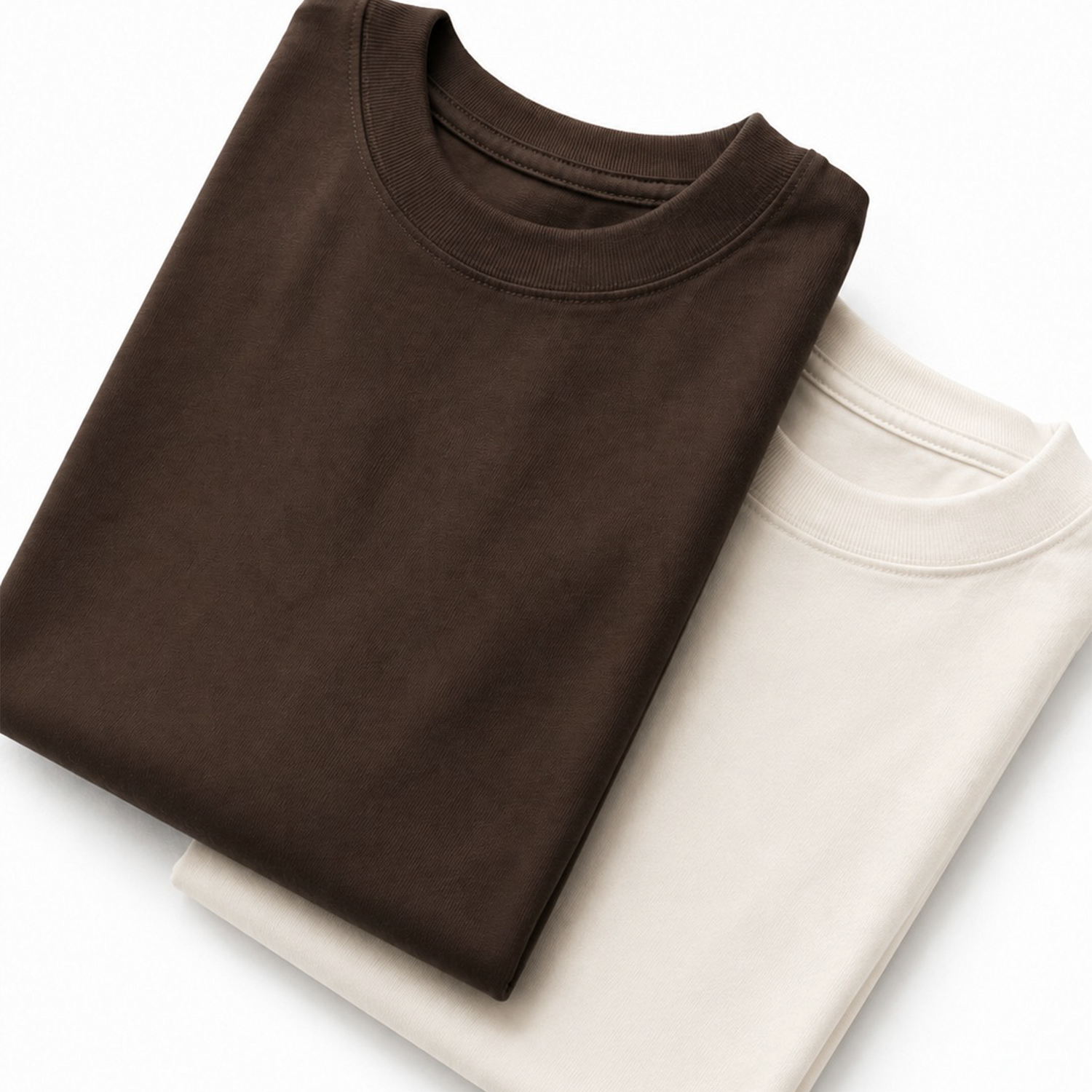 Camisetas oversize de algodón de alto gramaje en colores neutros (marrón chocolate y crudo), doblando con acabado premium para la colección de básicos esenciales de MAFA